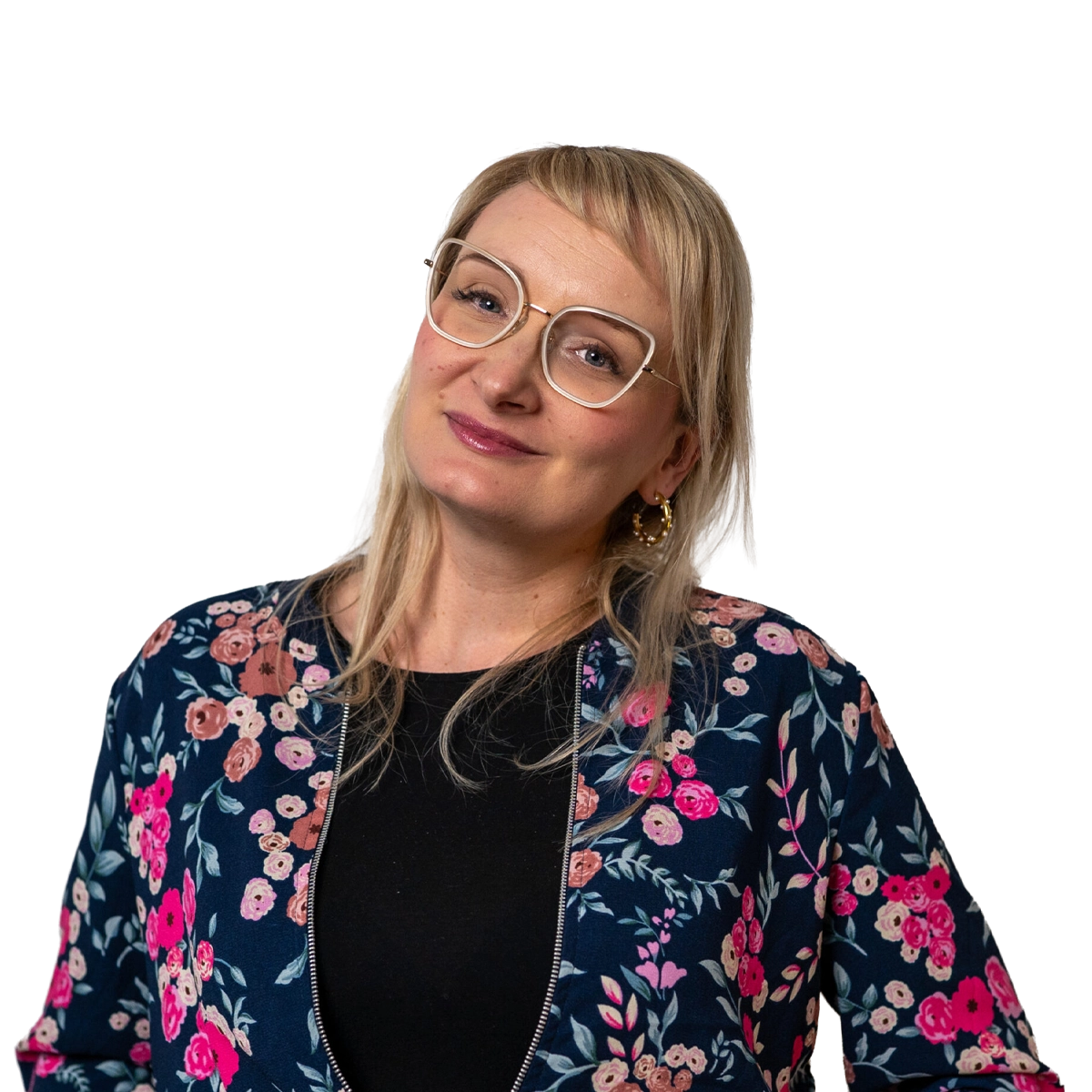 Auf dem Bild ist eine weibliche Person zu sehen die im Porträtmodus in die Kamera blickt. Die Person hat lange blonde Haare und trägt eine Brille. Die Person hat eine bunte Jacke und ein schwarzes T-Shirt an.