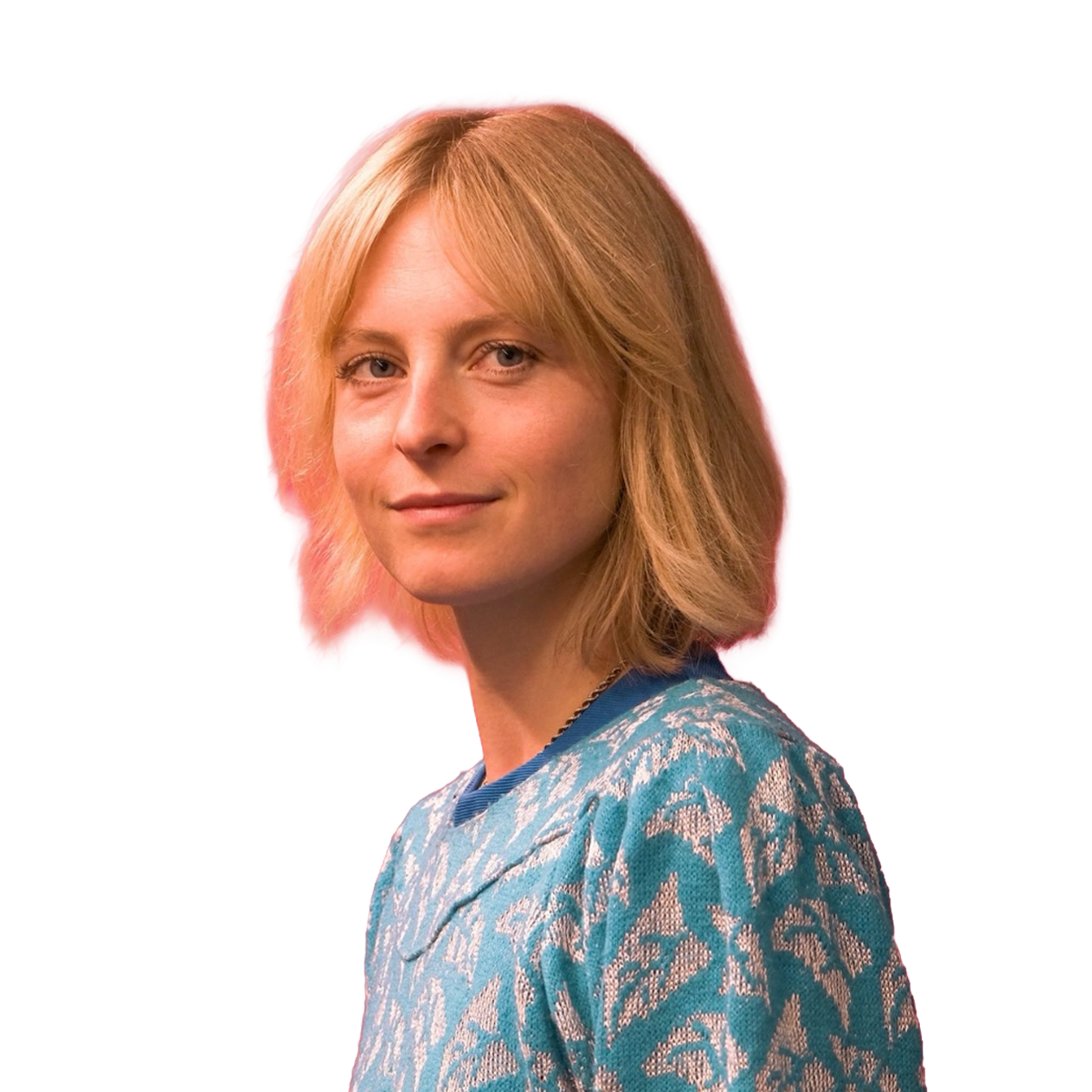 Auf dem Bild ist eine weibliche Person zu sehen die im Porträtmodus in die Kamera blickt. Die Person hat kurze blonde Haare und einen hellblau-weißen Pullover an.